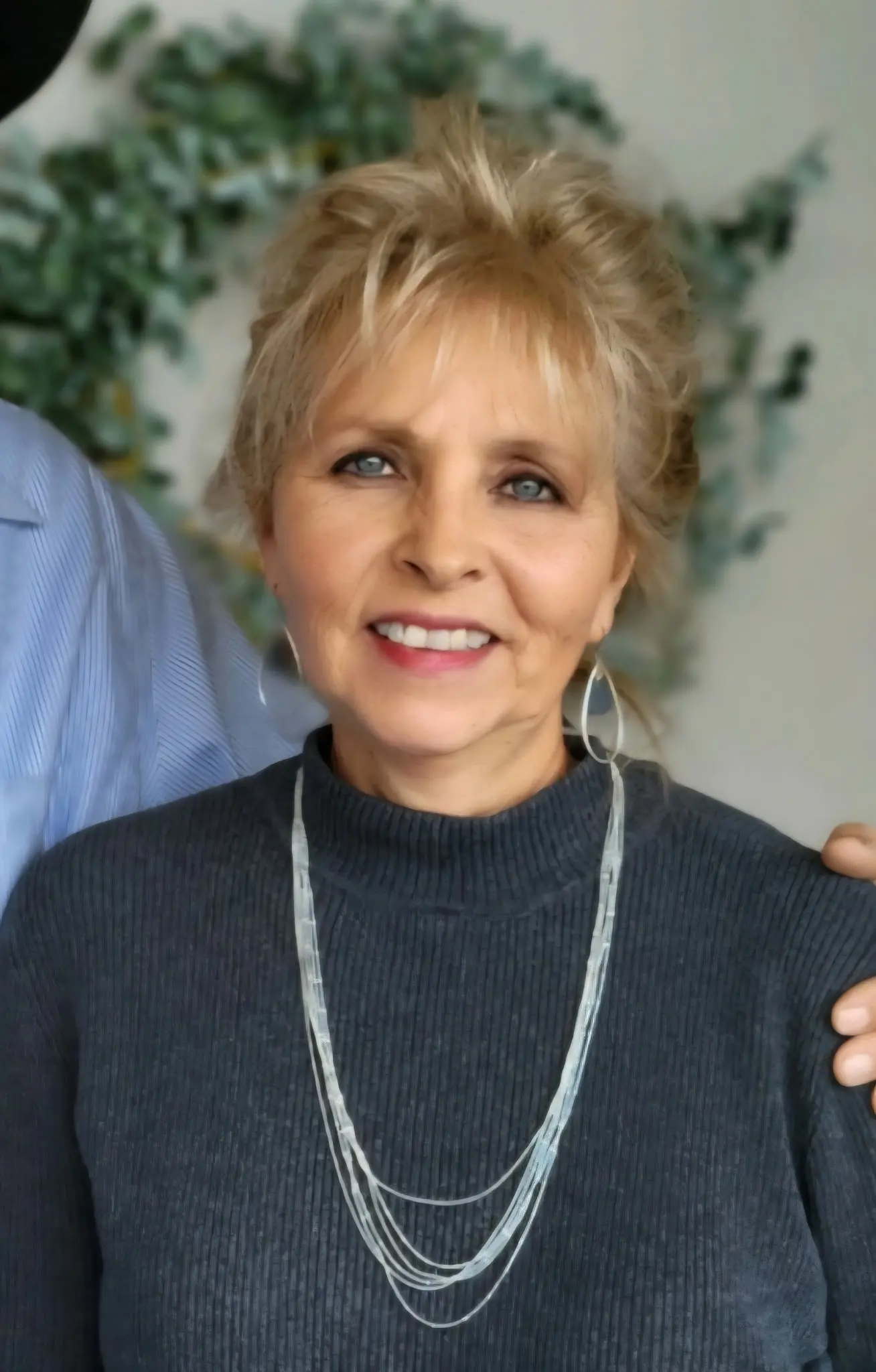 Smiling woman with short blonde hair in a dark sweater and necklace.