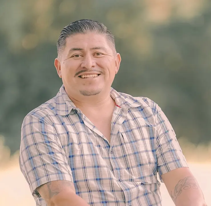Smiling man in a casual plaid shirt outdoors.