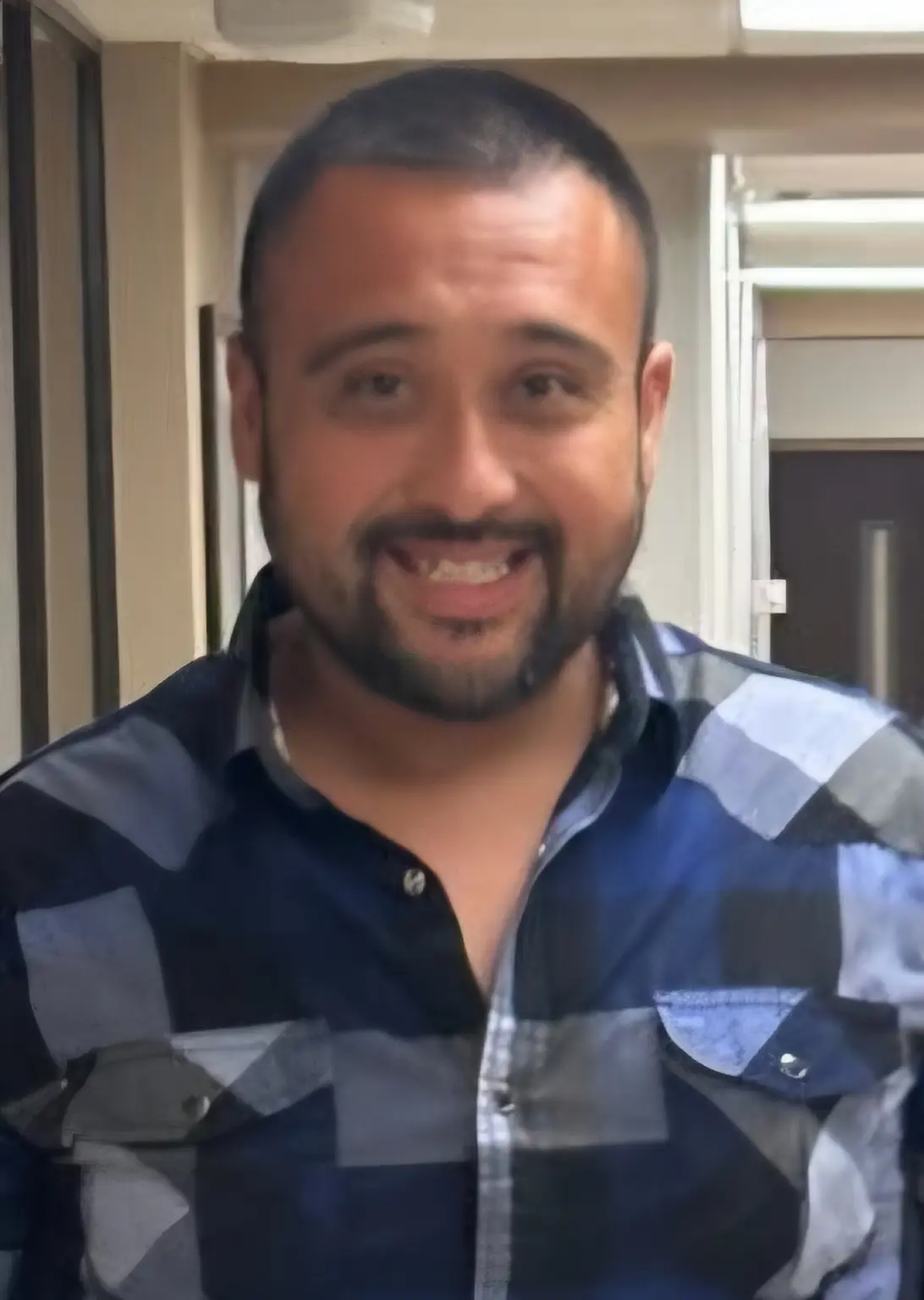 Smiling man in a checkered shirt indoors.