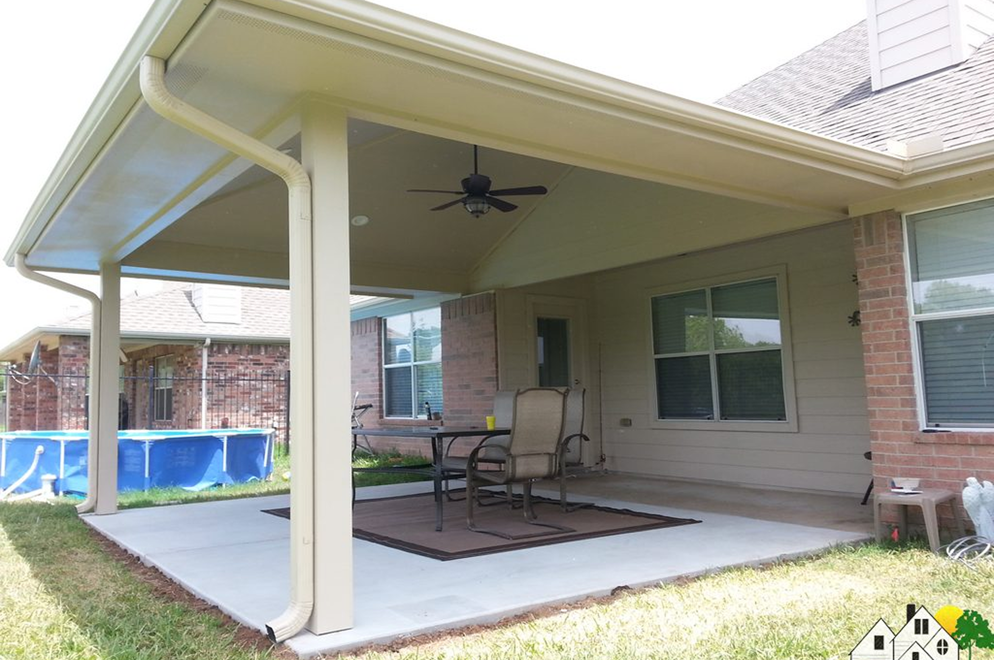 Covered patio with chairs and a ceiling fan beside a pool.