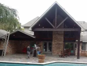 A backyard pool with a brick house and wooden beams.