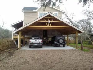 Two vehicles parked under a wooden carport attached to a house.
