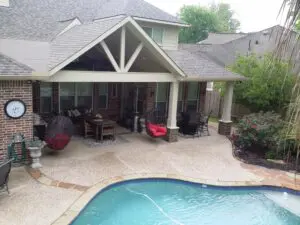 A backyard patio with a swimming pool and covered seating area.