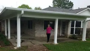 Woman standing under a porch in front of a brick house.