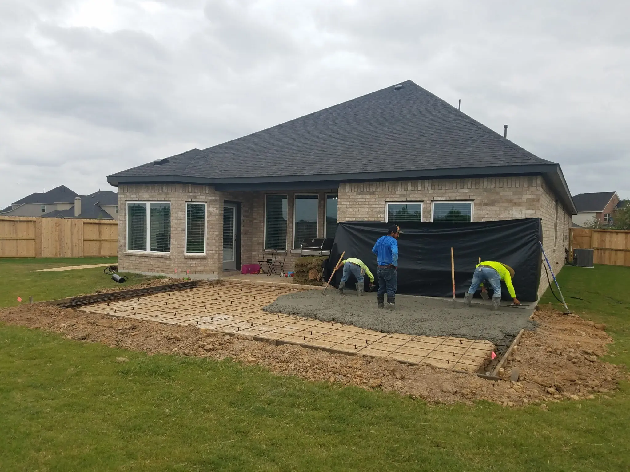 Two people working on a backyard patio in front of a single-story house with a gray roof.