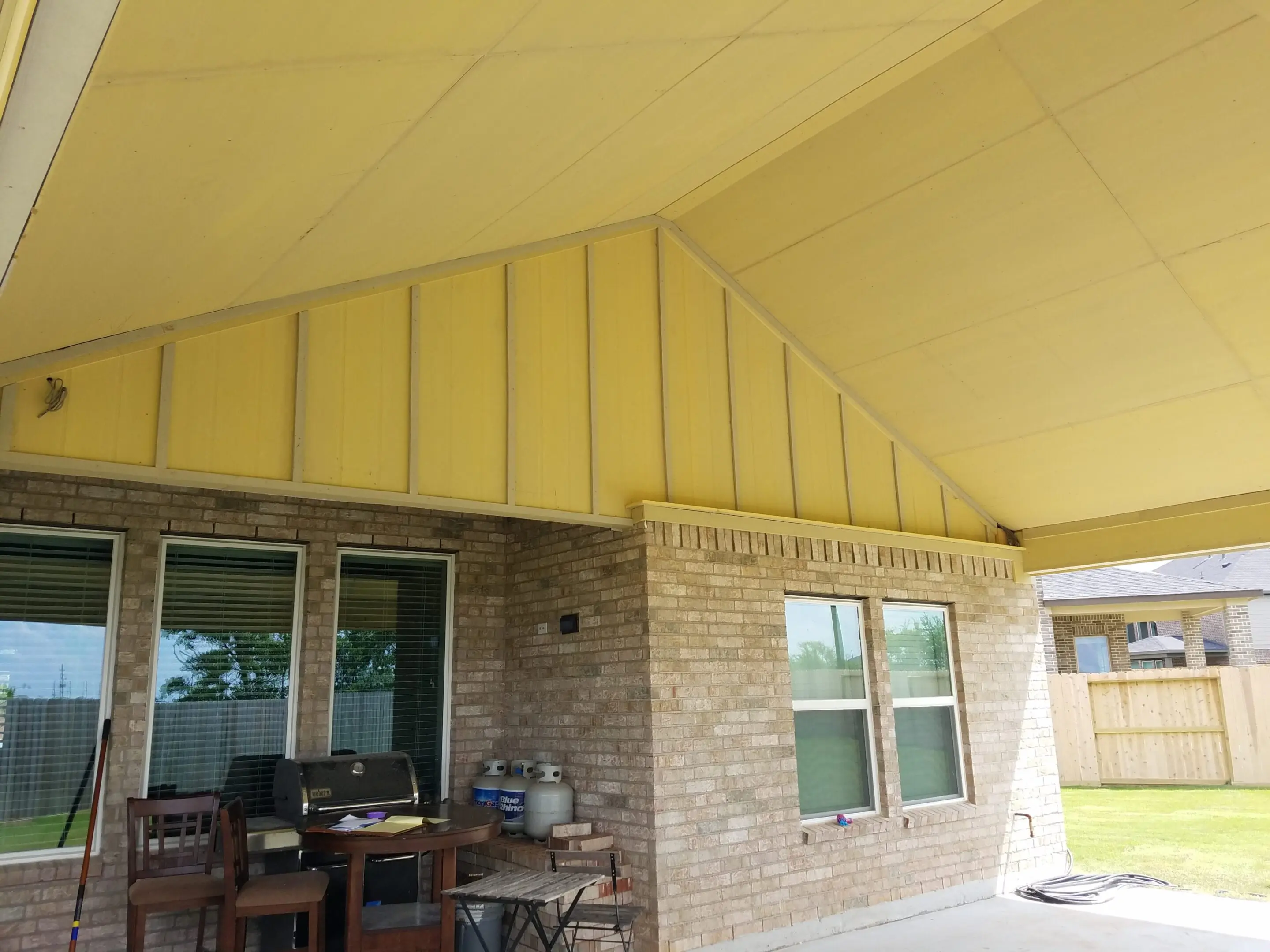Covered patio with yellow ceiling panels and brick walls.