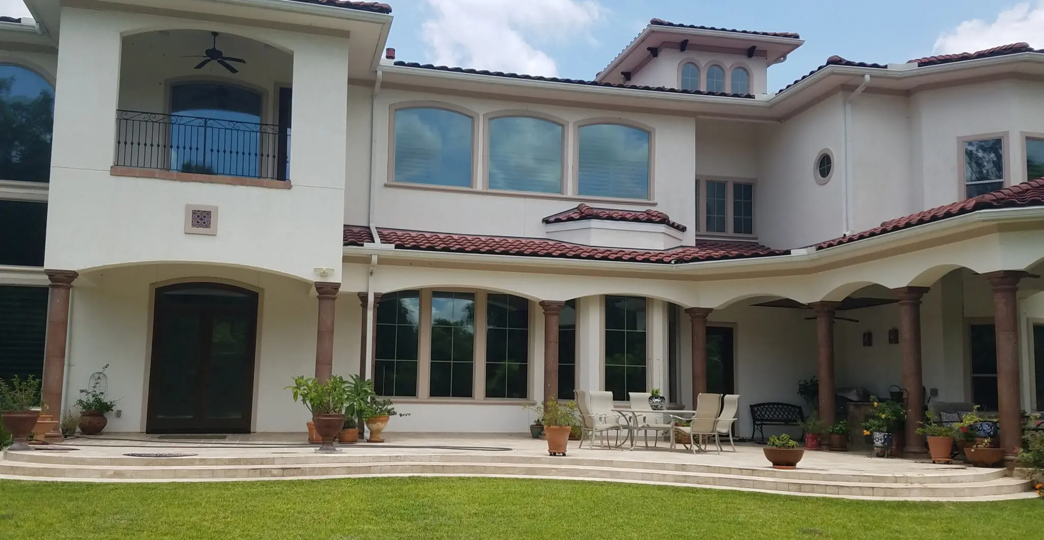 Large beige two-story house with arched windows and patio furniture.