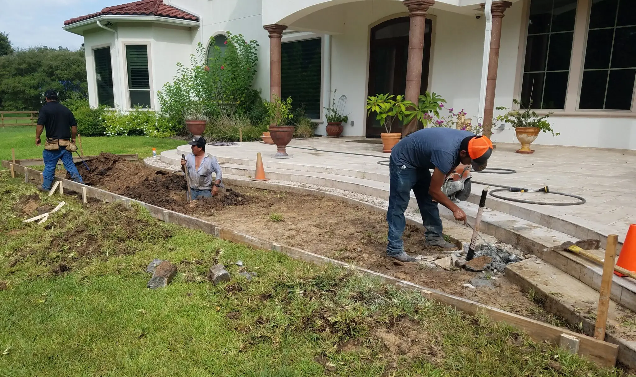 Two men working on a garden or patio construction project outside a house.