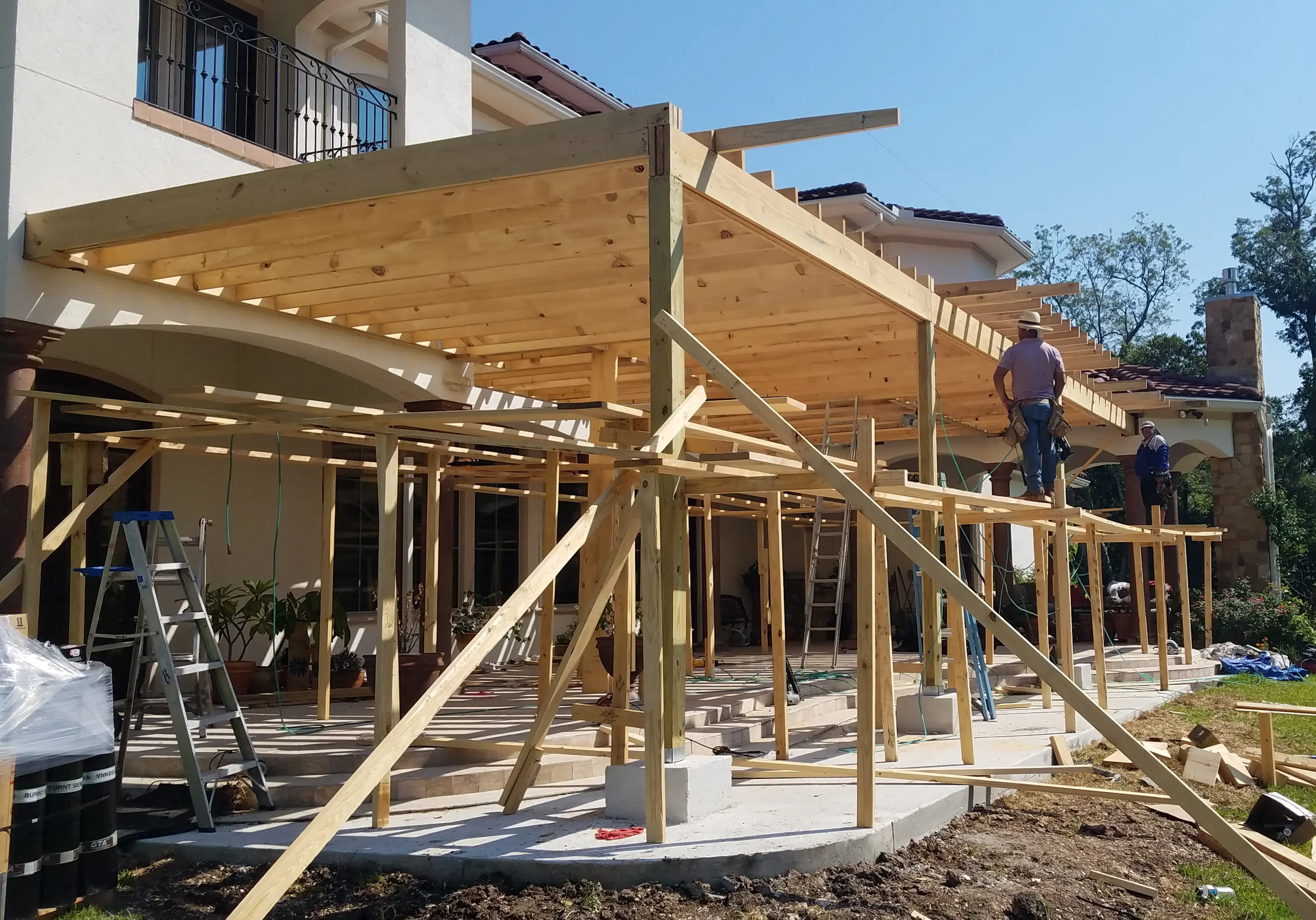 Construction workers build a wooden pergola outside a house.