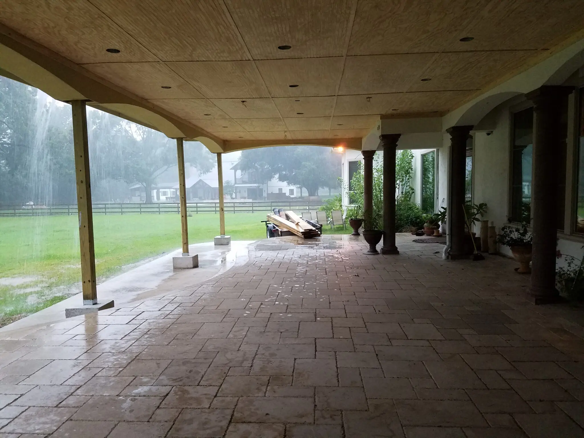 Covered patio with stone flooring overlooking a grassy yard and distant hills.
