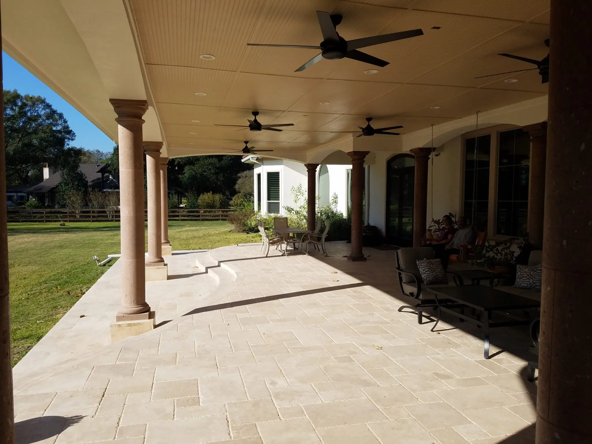 Spacious outdoor patio with ceiling fans and stone flooring.