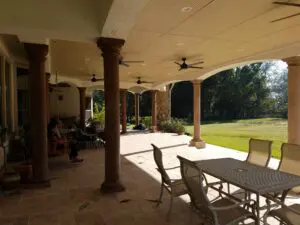 Spacious outdoor patio with large columns and seating area overlooking a green lawn.