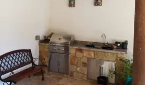 Outdoor kitchen with grill, sink, and stone countertop.
