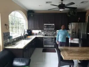Man standing in modern kitchen with dark cabinets and large window.