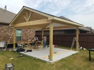 Workers building a wooden porch frame on a house exterior.