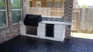 Outdoor kitchen with built-in grill and storage, covered with a black grill cover.