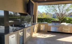Modern outdoor kitchen with stainless steel appliances and scenic garden view.
