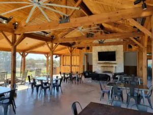 Spacious wooden pavilion with tables, chairs, and a fireplace under a peaked roof.