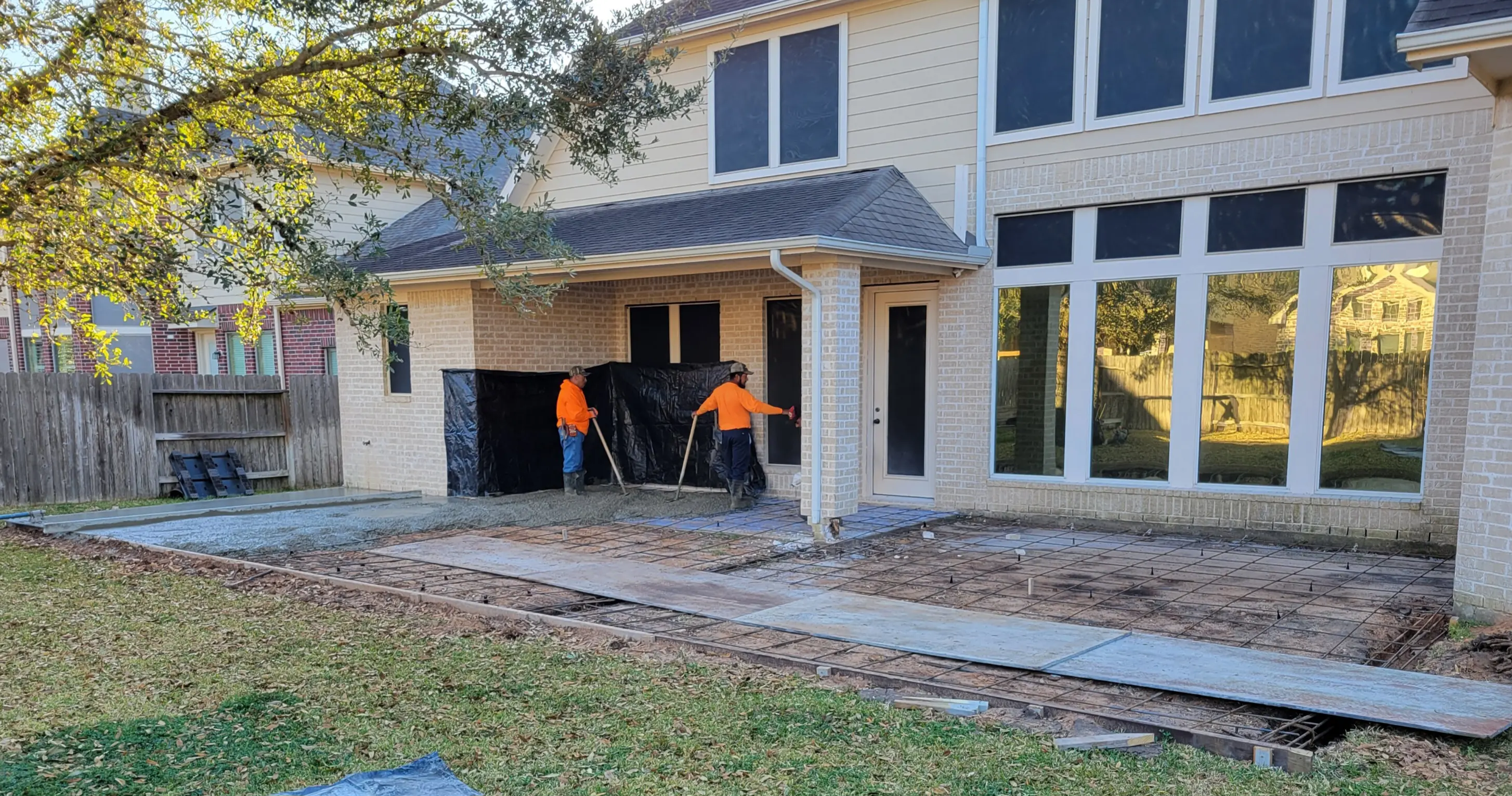 Workers preparing concrete for a driveway in front of a house.