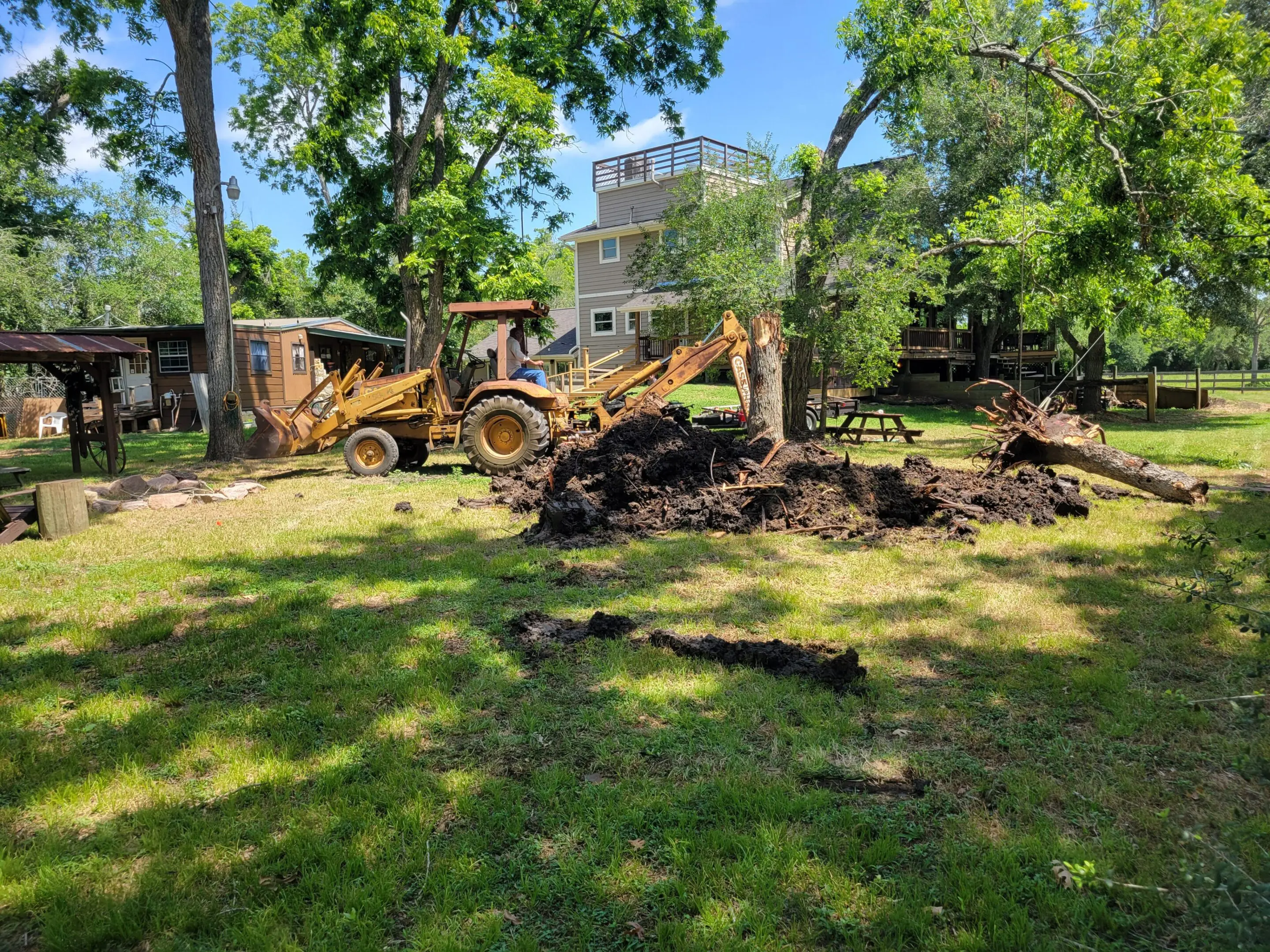 Excavator digging soil in a green garden area near buildings.