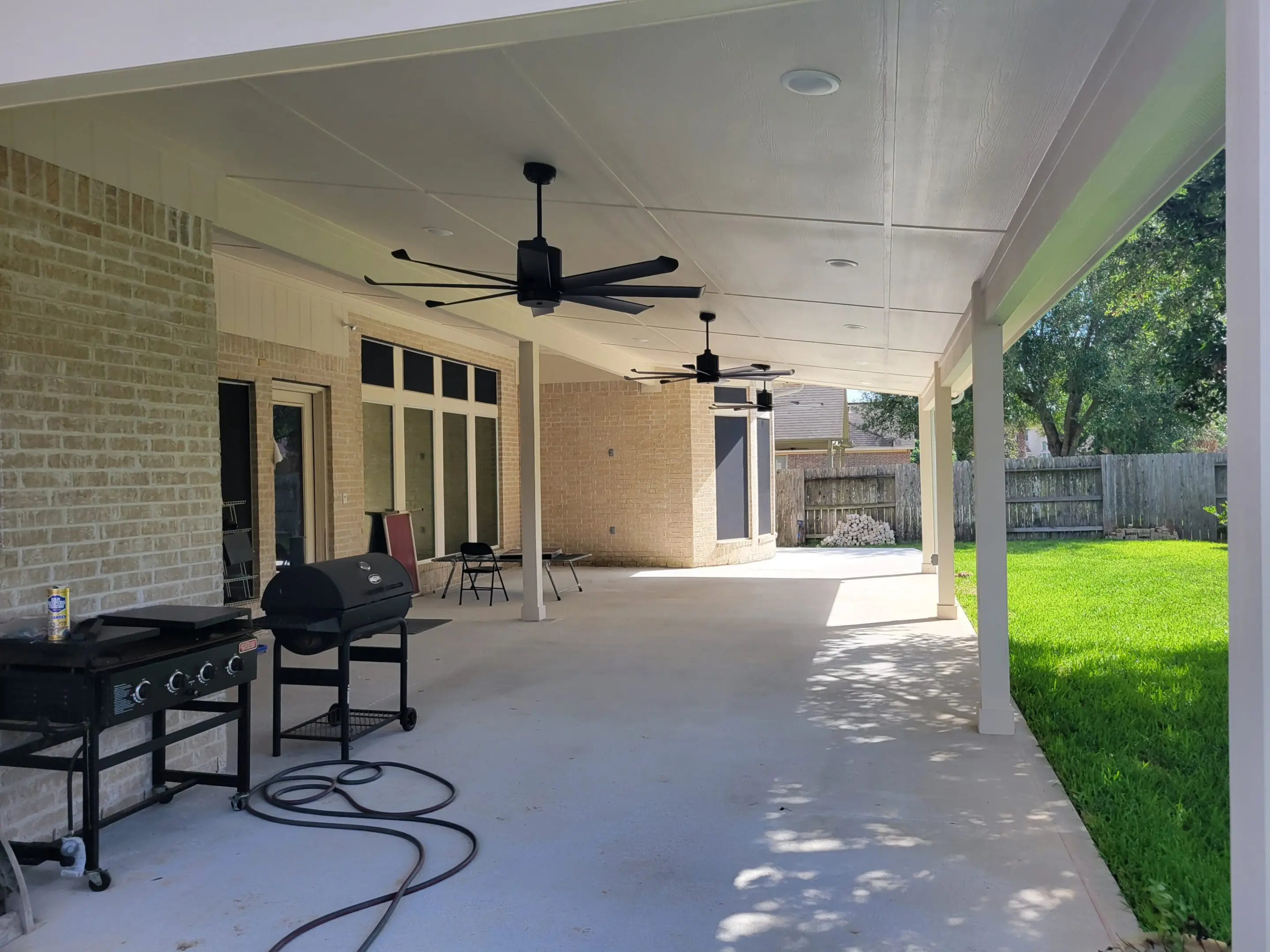 Spacious covered patio with ceiling fans and a grill overlooking a green lawn.