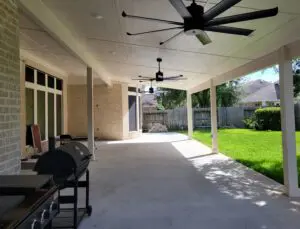 Spacious covered patio with ceiling fans and a barbecue grill overlooking a green lawn.