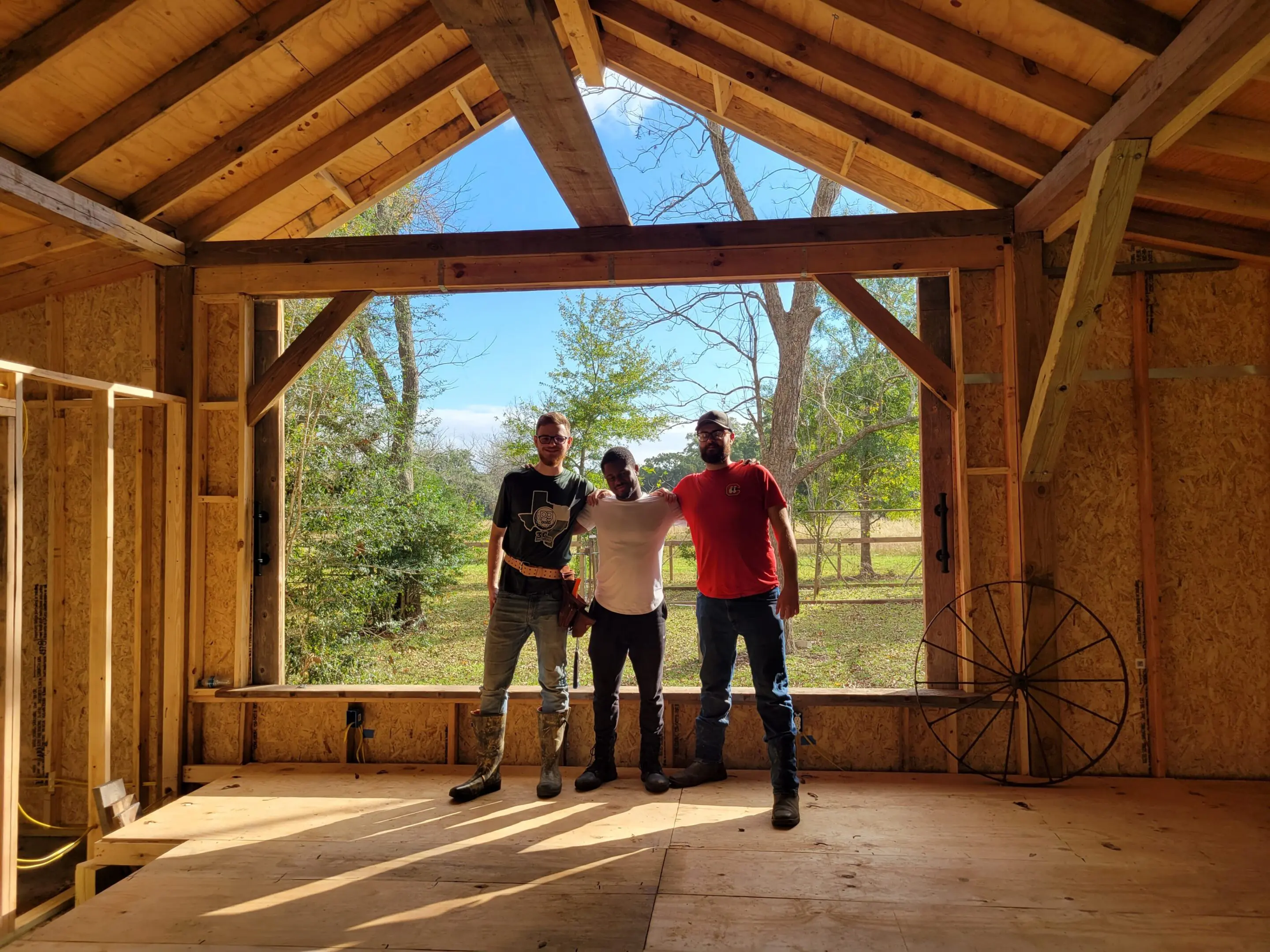 Three people standing inside a wooden structure with a scenic outdoor view.
