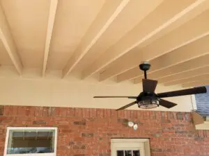 Ceiling fan mounted on a white-beamed patio ceiling with brick walls.