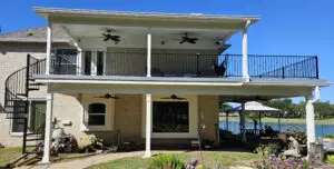 Two-story house with an outdoor balcony and ceiling fans under a clear blue sky.