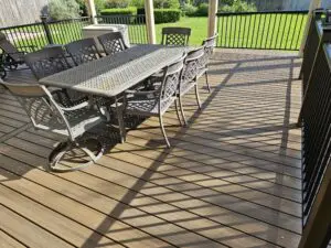 Outdoor dining table and chairs casting shadows on a wooden deck.