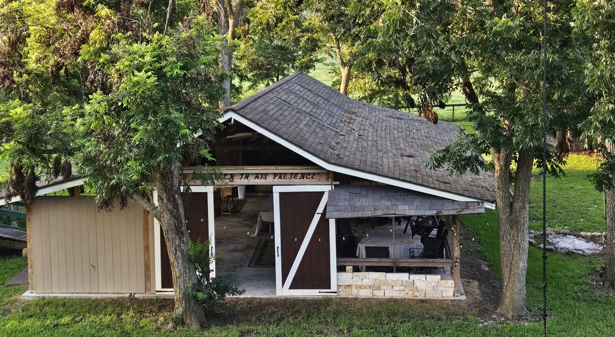 Rustic barn with open doors surrounded by greenery in a peaceful setting.