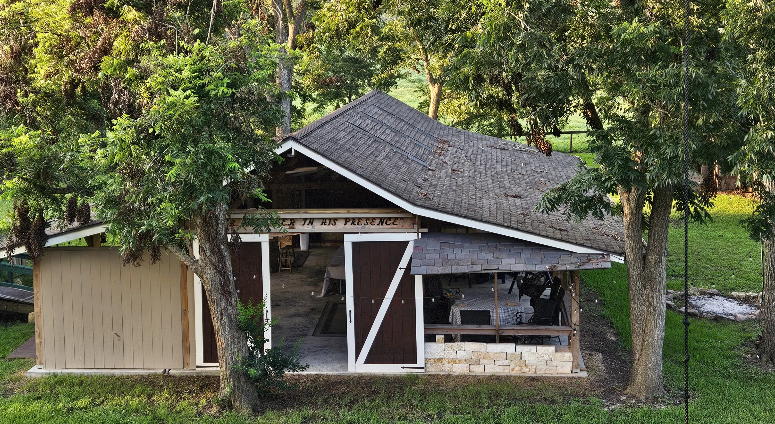Rustic barn with open doors surrounded by greenery in a peaceful setting.
