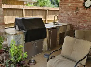 Outdoor kitchen area with grill and sink under a covered patio.