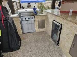 Outdoor kitchen with grill and built-in refrigerator under a canopy.