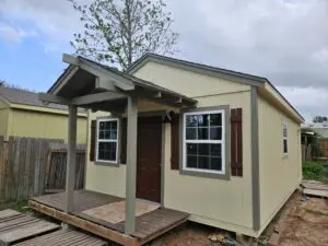 A small, beige house with a wooden porch under a cloudy sky.