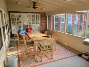 Two people relaxing on a screened porch with wooden furniture.