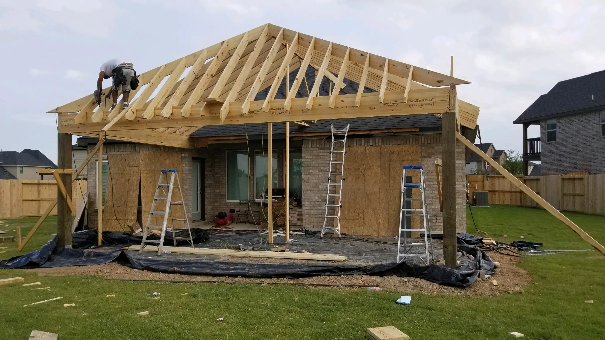 House under construction with wooden roof framing and ladders.