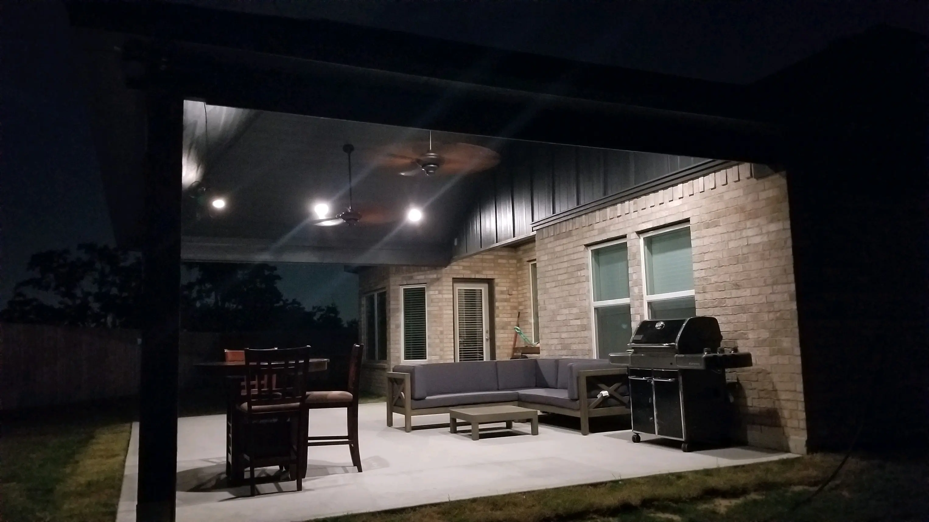 Cozy outdoor patio with seating and grill under warm lighting at night.