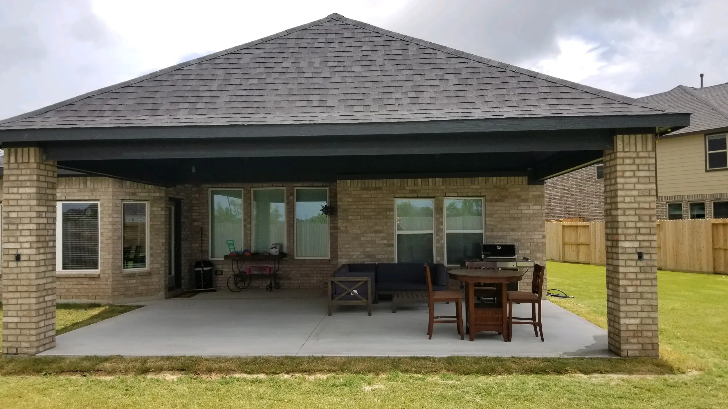 Covered patio with outdoor furniture and grill in a backyard.