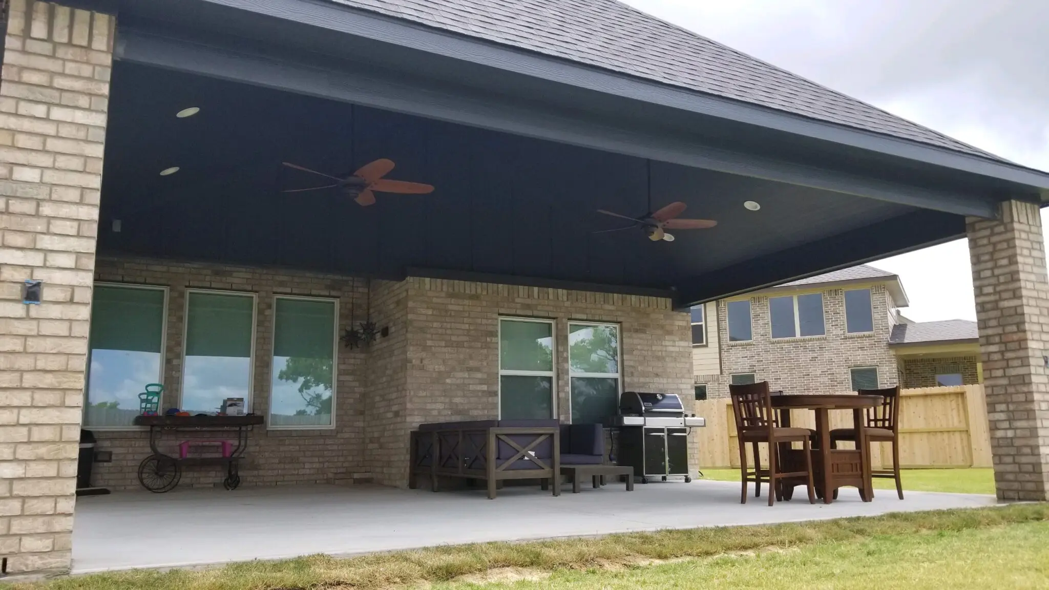 Covered patio with ceiling fans and outdoor furniture in a backyard.