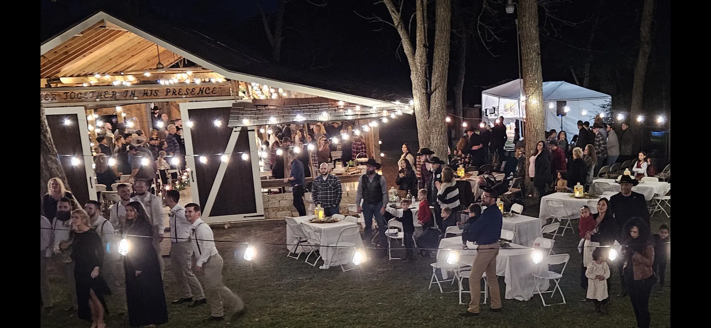 Outdoor evening party with string lights and people socializing around tables.