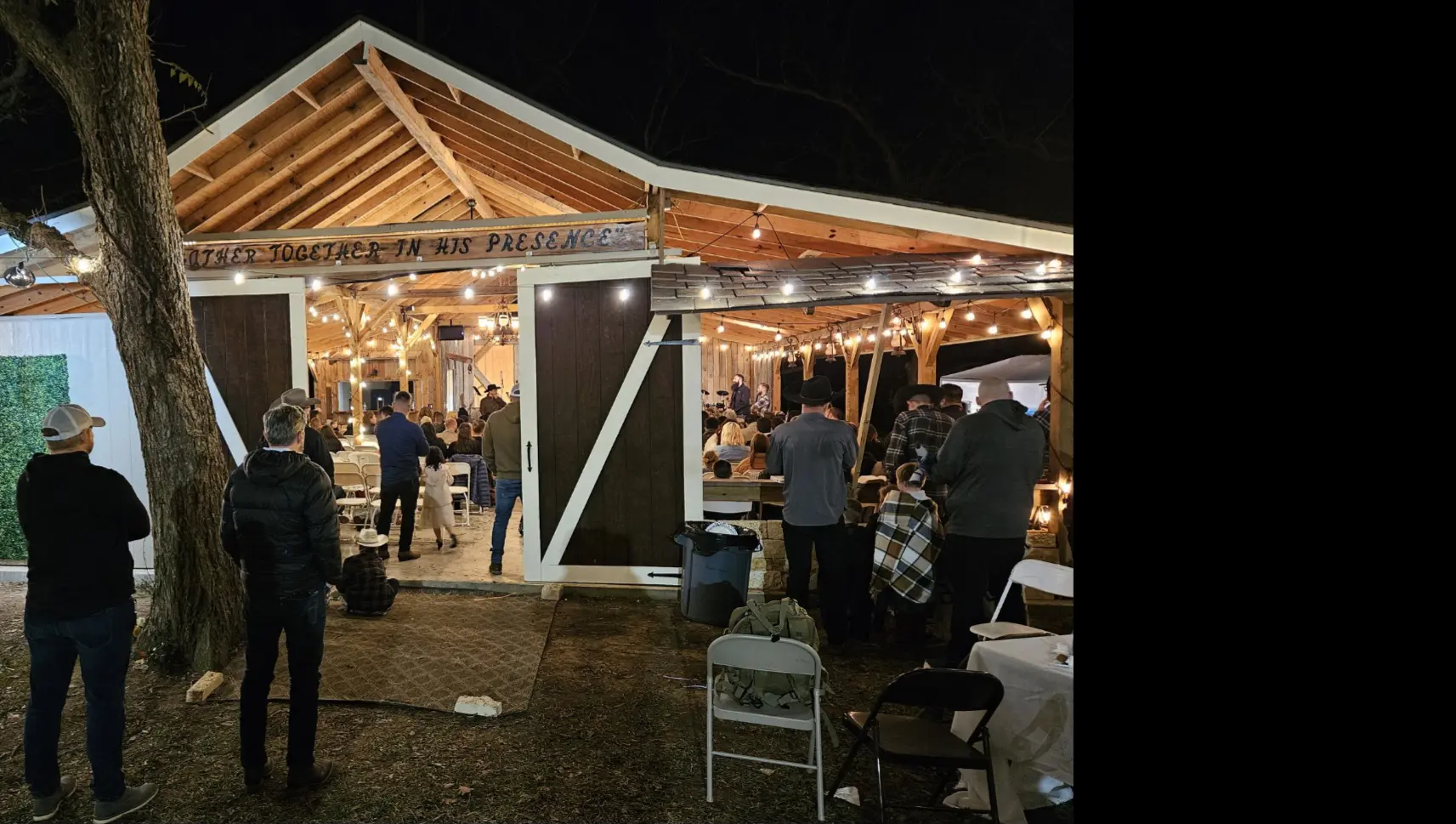 People gather under a warmly lit outdoor pavilion at night.