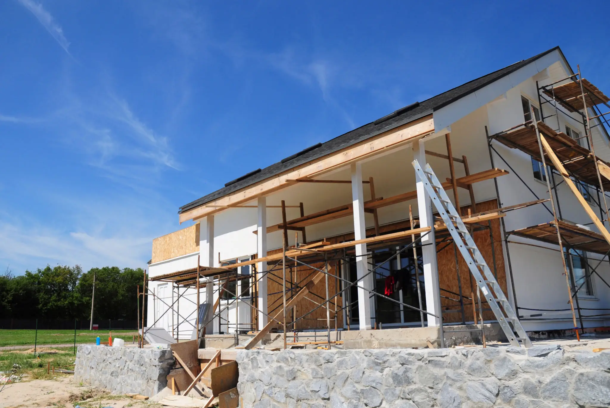 House under construction with scaffolding and clear blue sky.